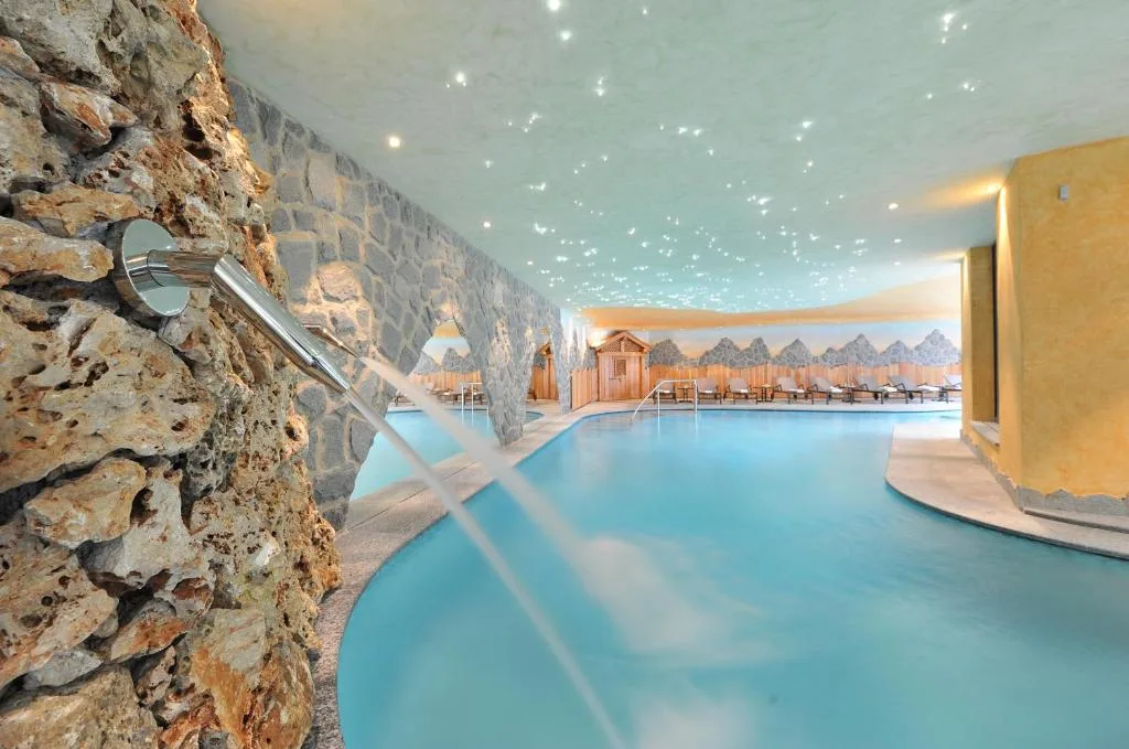 Piscina coperta con parete in pietra, cascata d'acqua e soffitto stellato