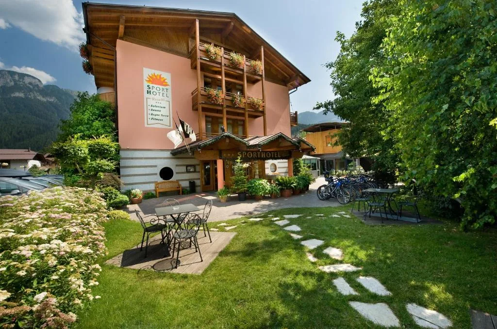 Facciata dell'hotel con giardino fiorito, tavolini in ferro e rastrelliera biciclette
