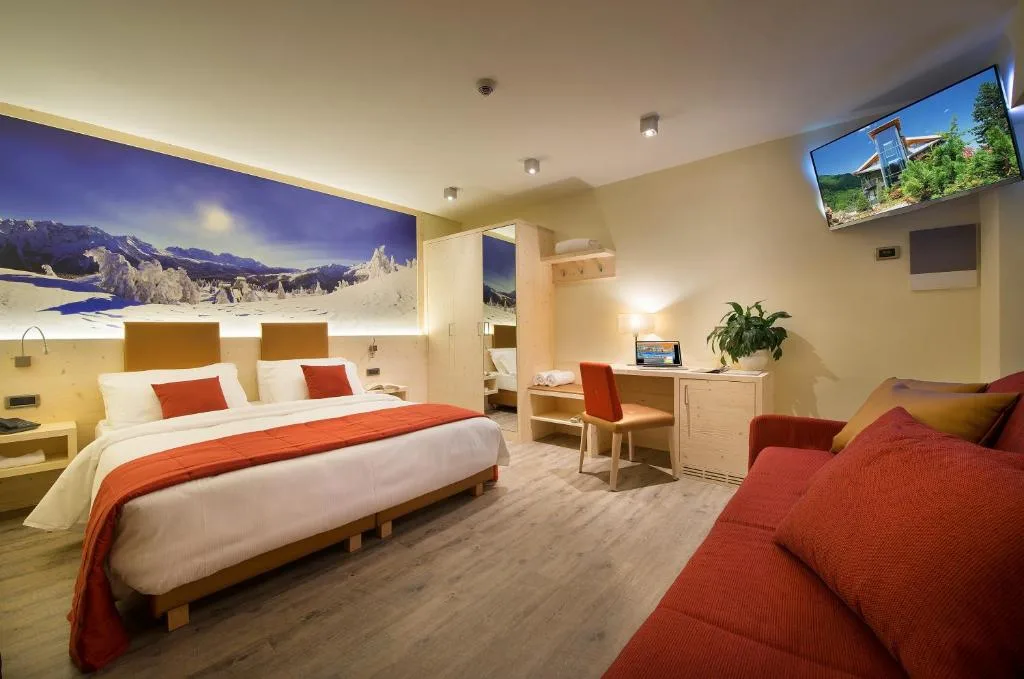 Camera contemporanea con letto matrimoniale, divano rosso e stampa panoramica delle montagne