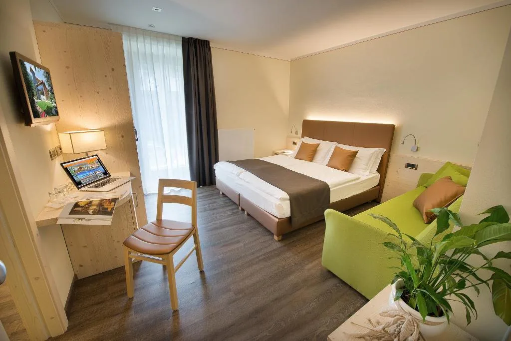 Camera moderna con letto matrimoniale, divano verde e scrivania con laptop