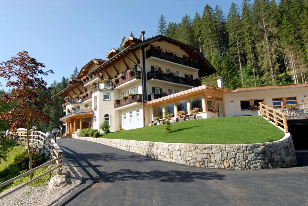 Ingresso dell'hotel di montagna con vialetto e muretto in pietra circondato da pini