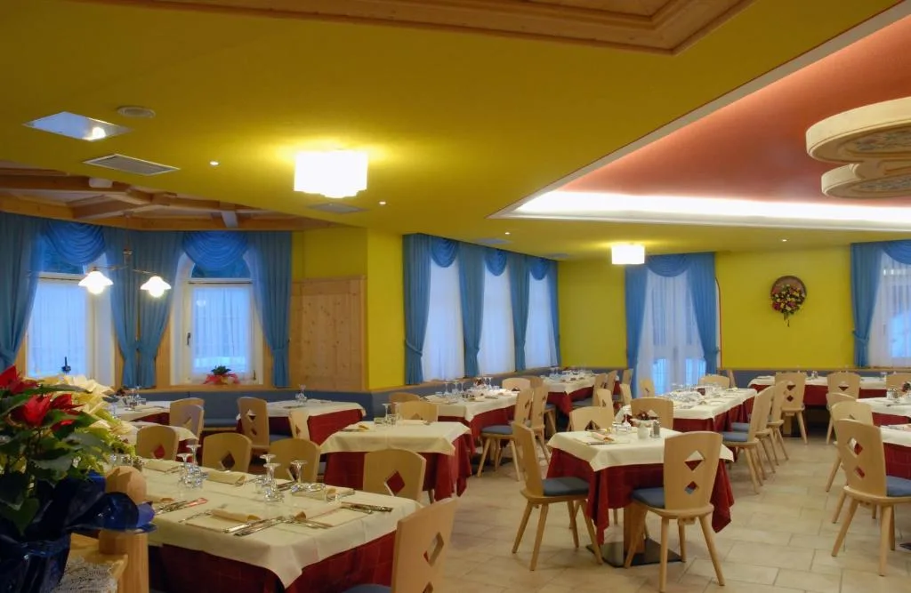 Ampia sala da pranzo con pareti gialle, tende blu e tavoli apparecchiati