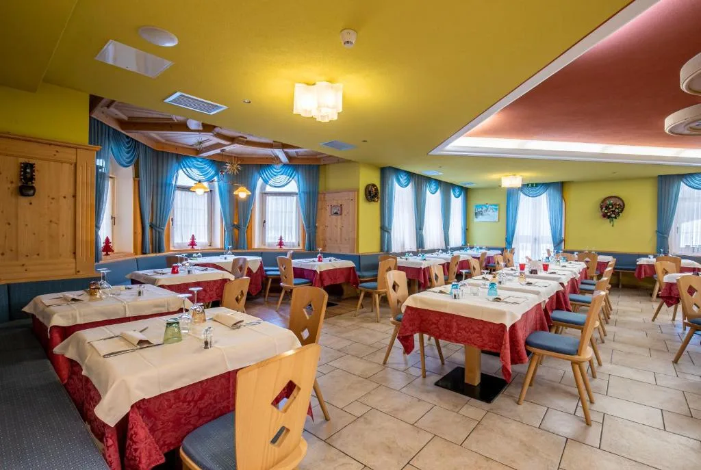 Sala ristorante con tavoli apparecchiati, tovaglie rosse e tende blu