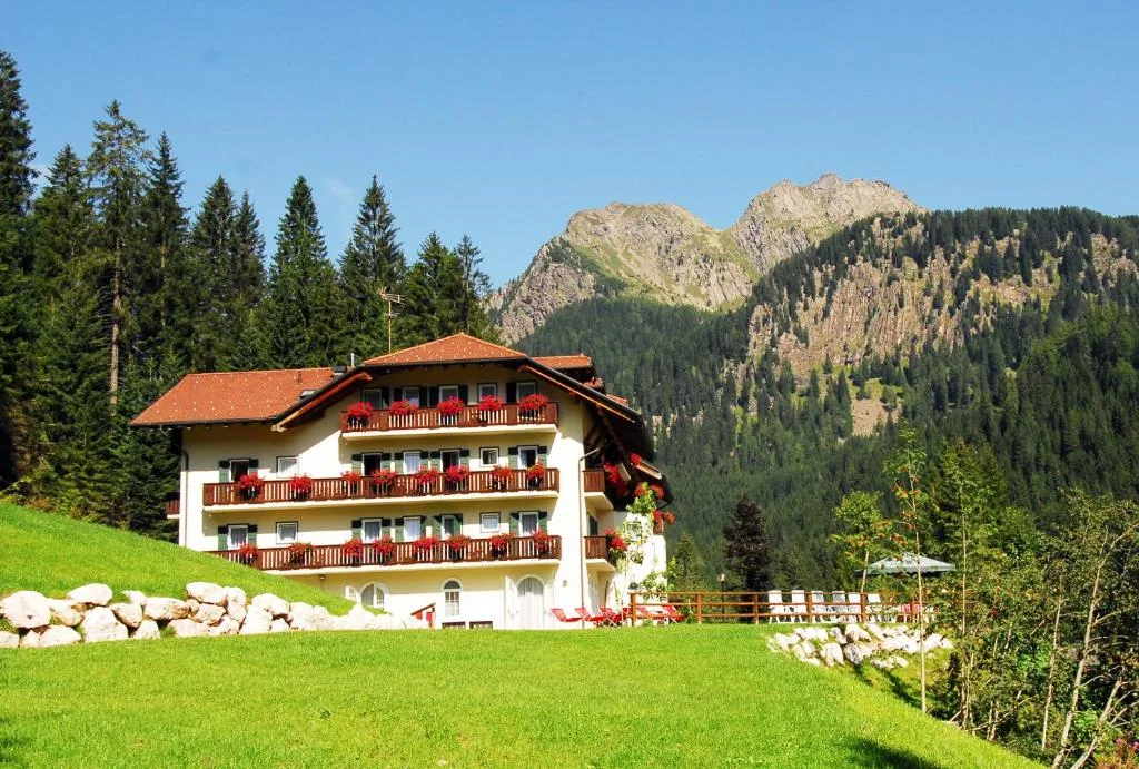 Hotel con balconi fioriti su prato verde con montagne rocciose sullo sfondo
