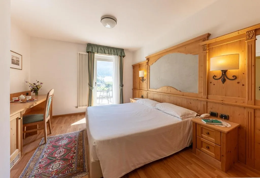 Camera con letto matrimoniale, testiera in legno decorato e balcone