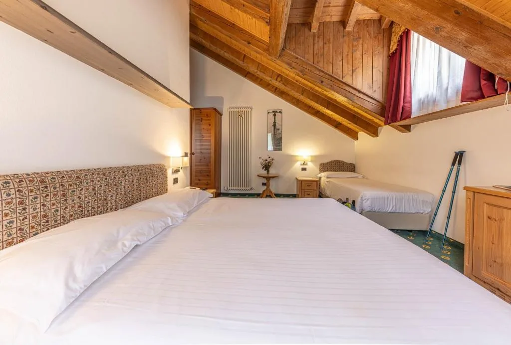 Camera mansardata con letto matrimoniale, letto singolo e travi in legno