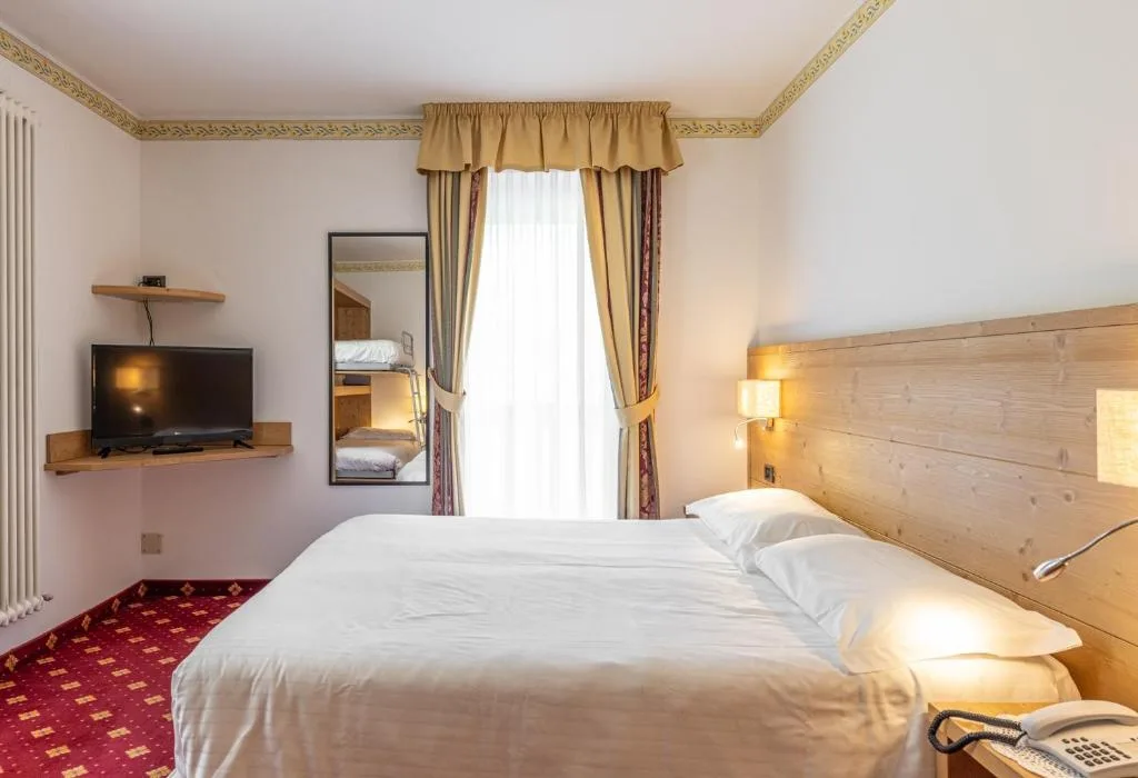 Camera con letto matrimoniale, TV e tende dorate su moquette rossa