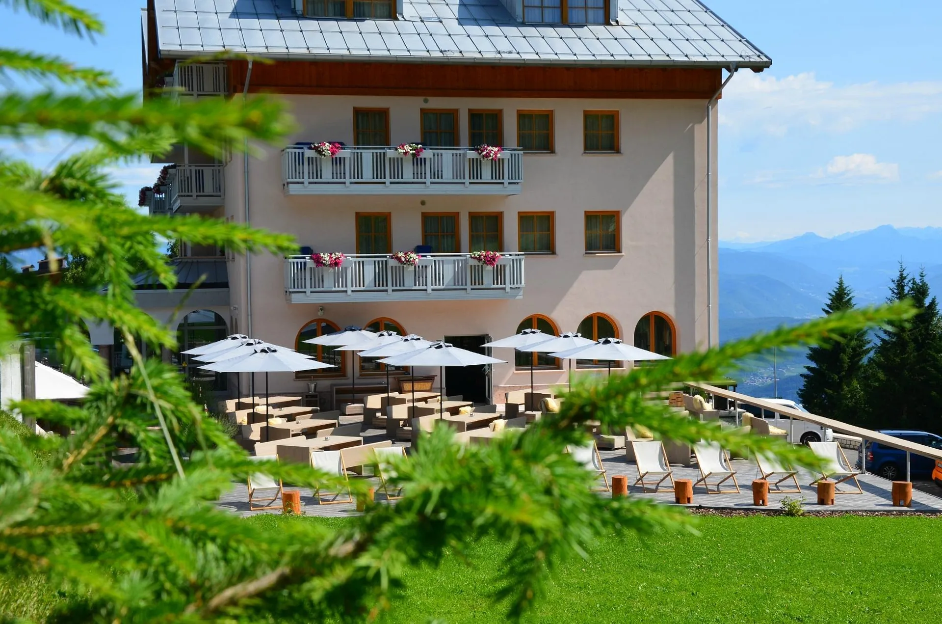 Facciata dell'hotel in estate con balconi fioriti e vista sulle montagne