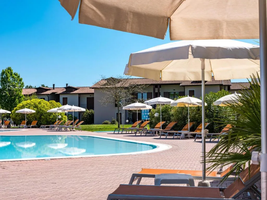 Vista sulla piscina con ombrelloni e lettini tra il verde del giardino