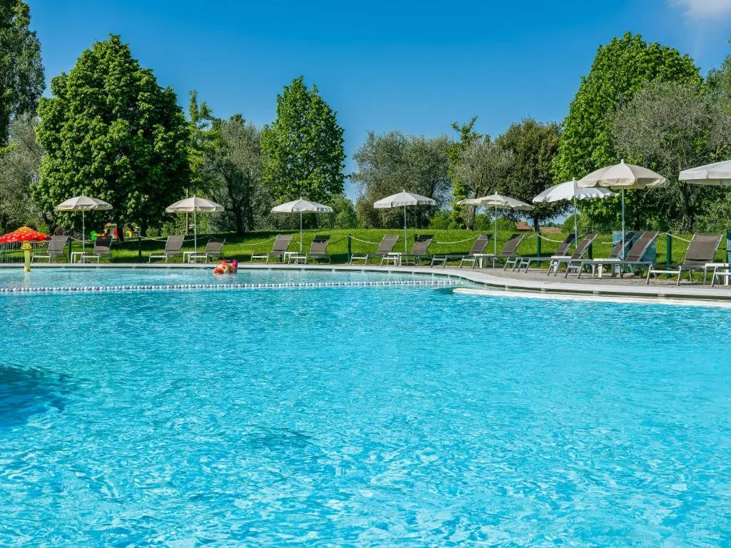 Grande piscina esterna con lettini e ombrelloni immersa nel verde