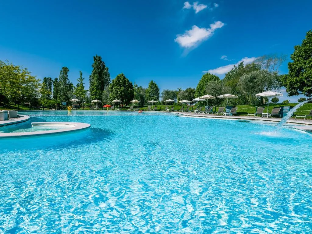 Ampia piscina con idromassaggio, getto d'acqua e ombrelloni tra gli alberi