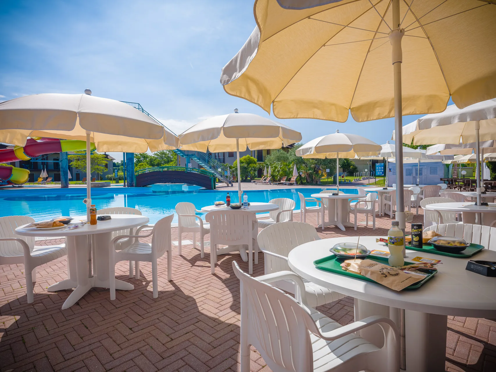 Area bar a bordo piscina con tavoli, sedie bianche e ombrelloni