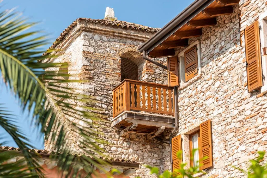 Dettaglio di edificio in pietra con balcone in legno e persiane color arancio