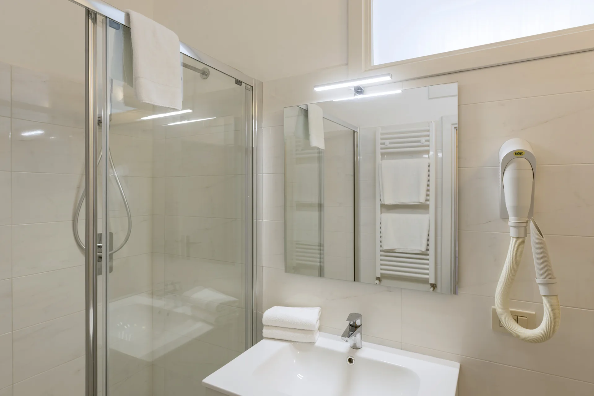 Bagno moderno con doccia in vetro, lavabo, specchio e asciugacapelli a parete