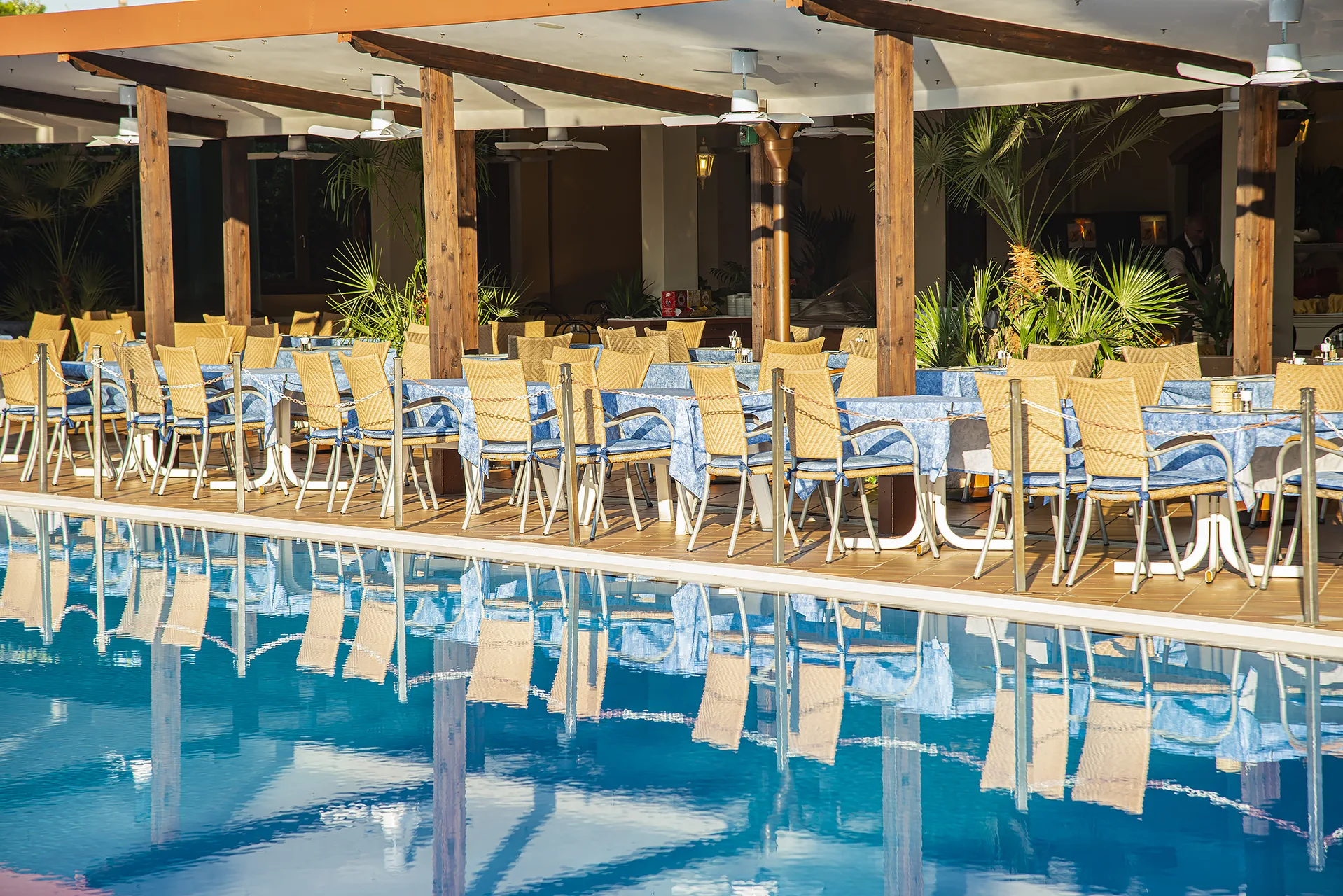 Ristorante all'aperto sotto pergolato in legno con tavoli affacciati sulla piscina