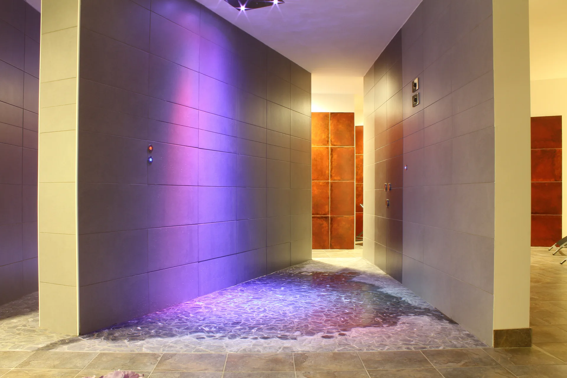 Area spa con doccia emozionale e giochi di luce viola su pareti in pietra