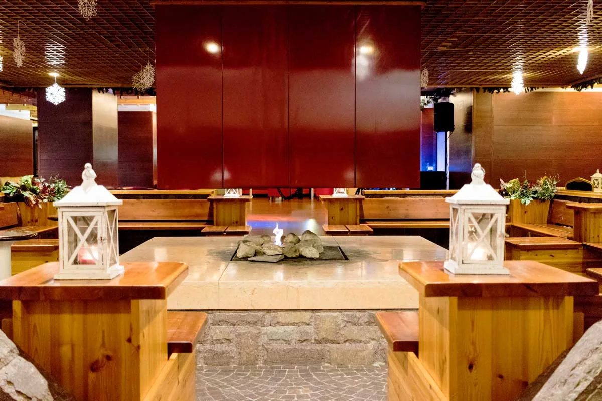 Sala con camino centrale in pietra, lanterne bianche e sedute in legno