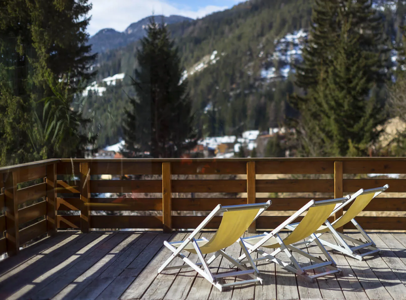 Terrazza in legno con sdraio gialle e vista sulle montagne innevate e boschi di abeti