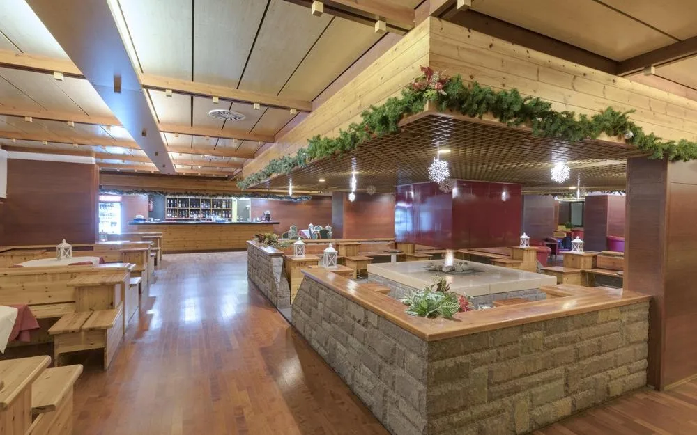 Ampia sala ristorante in stile alpino con tavoli in legno, camino centrale e decorazioni natalizie