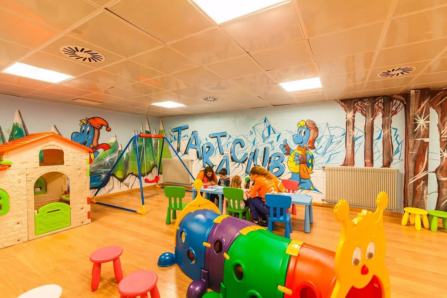 Sala giochi per bambini con casetta, scivoli colorati e pareti dipinte a tema