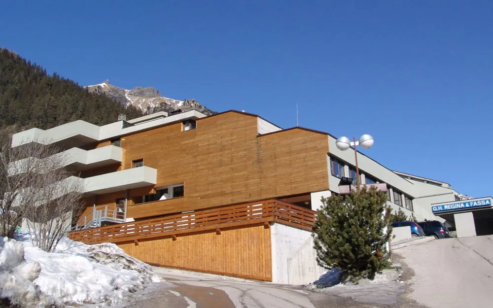 Esterno dell'hotel Regina & Fassa con facciata in legno e cielo azzurro sopra le montagne