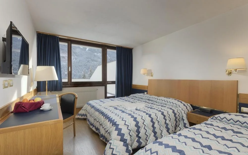 Camera matrimoniale con letto, scrivania, TV e finestra con vista sulle montagne innevate