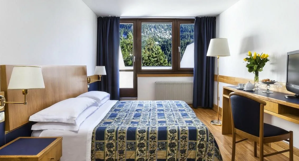 Camera luminosa con letto matrimoniale, scrivania in legno e finestra affacciata sui boschi