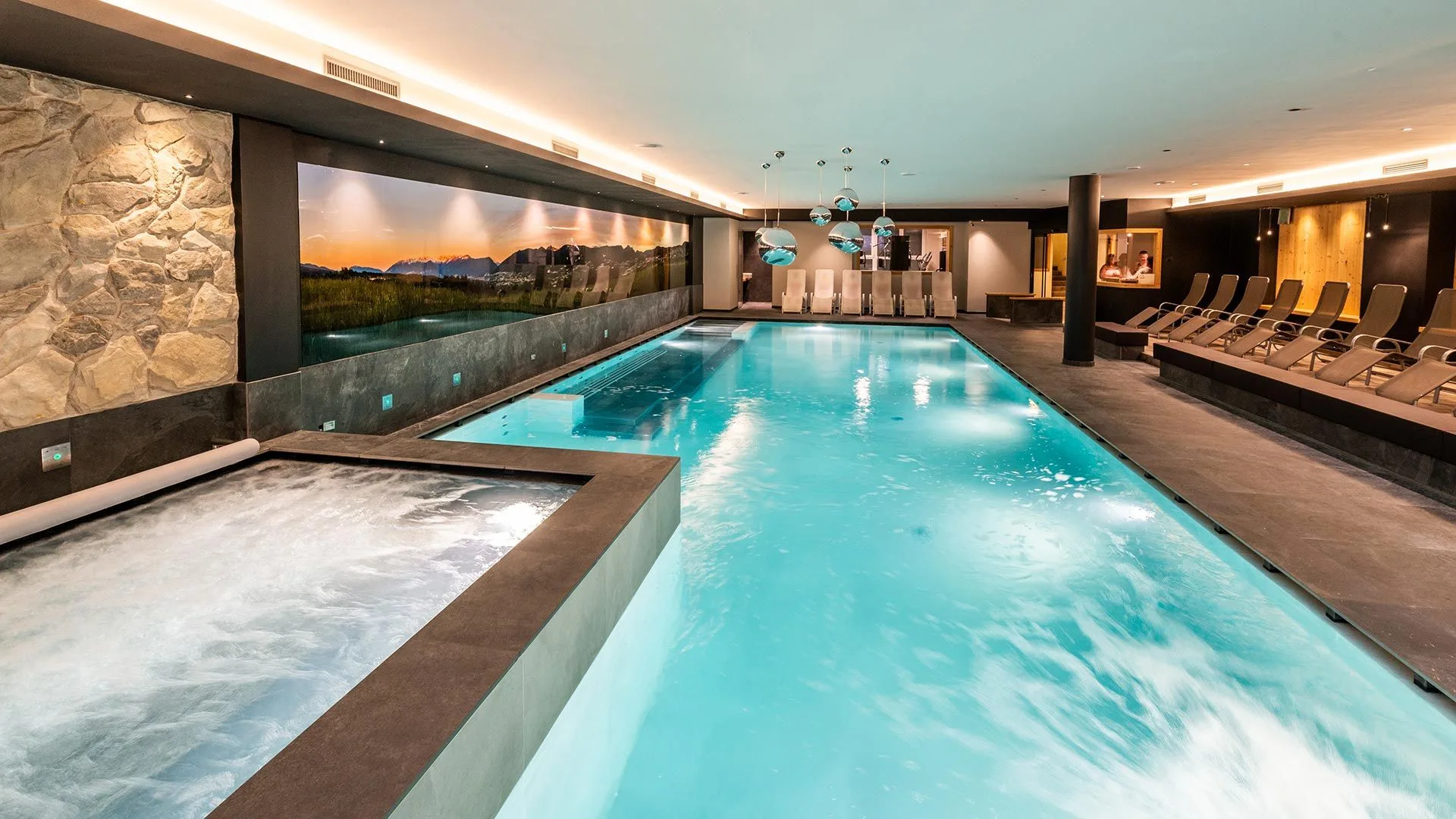 Piscina interna con idromassaggio, parete in pietra e lettini relax