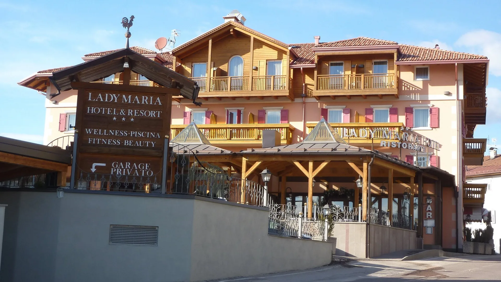 Esterno dell'Hotel Lady Maria con insegna, veranda e stile alpino di giorno