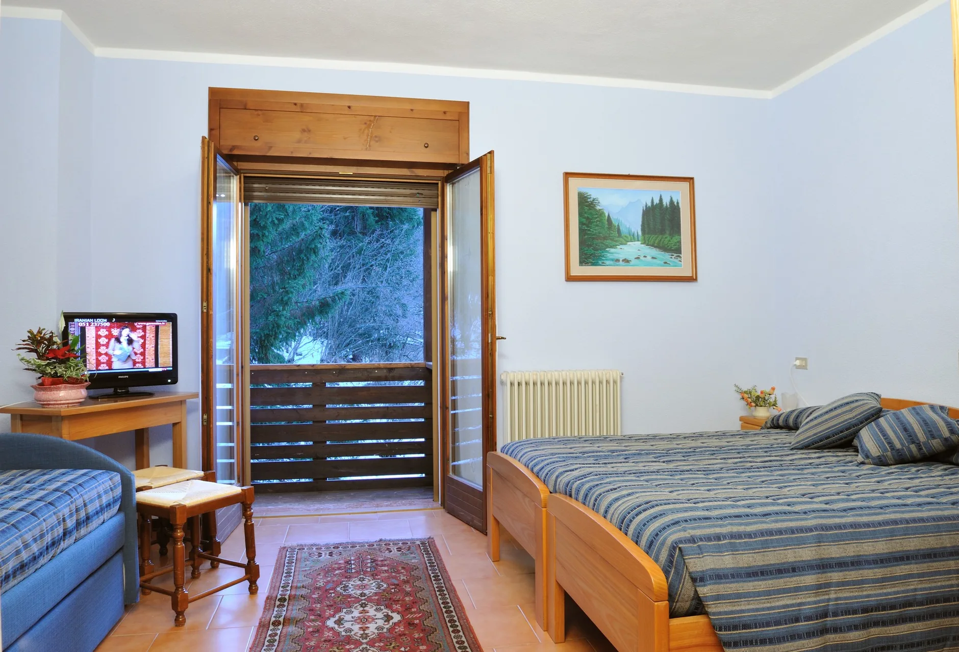 Camera dell'hotel con letto, TV, divano e balcone affacciato sul verde
