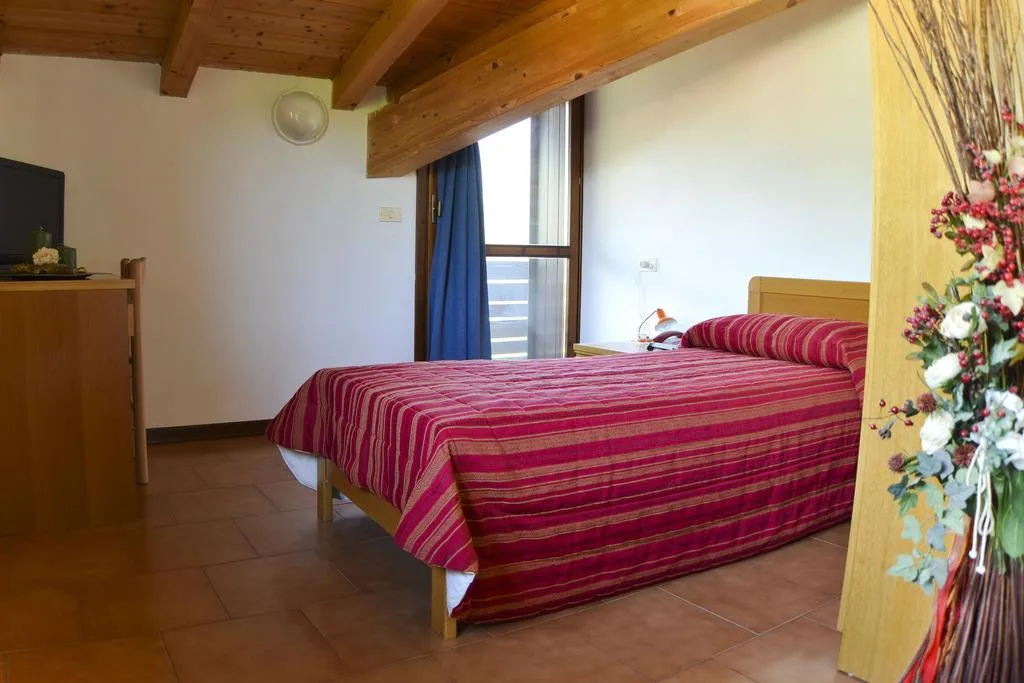 Camera mansardata con soffitto in travi di legno e letto matrimoniale rosso