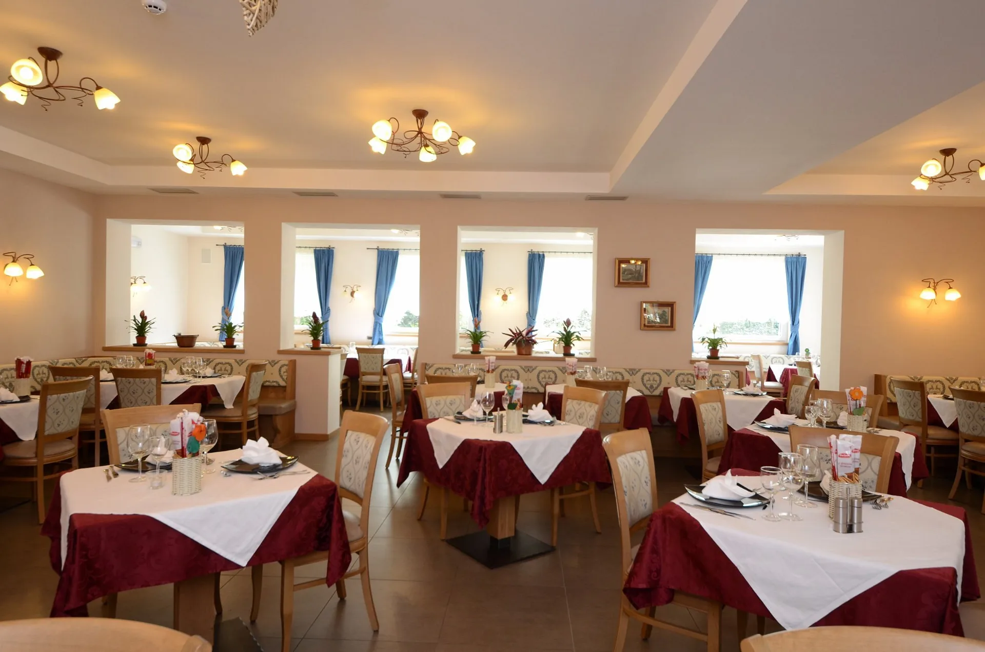 Sala ristorante luminosa con tavoli apparecchiati e tende blu alle finestre