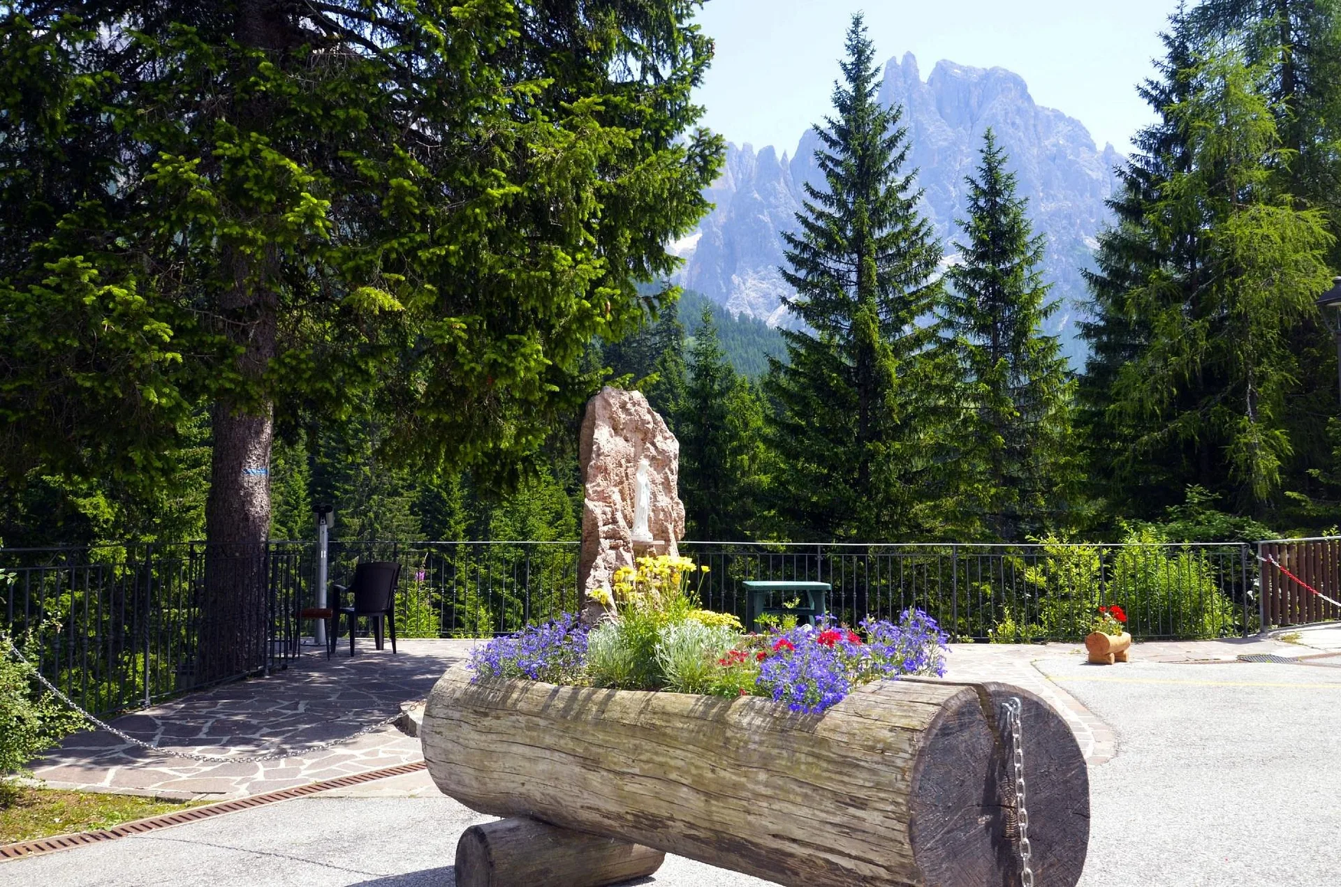 Terrazza fiorita con statua e vista sulle cime dolomitiche in estate