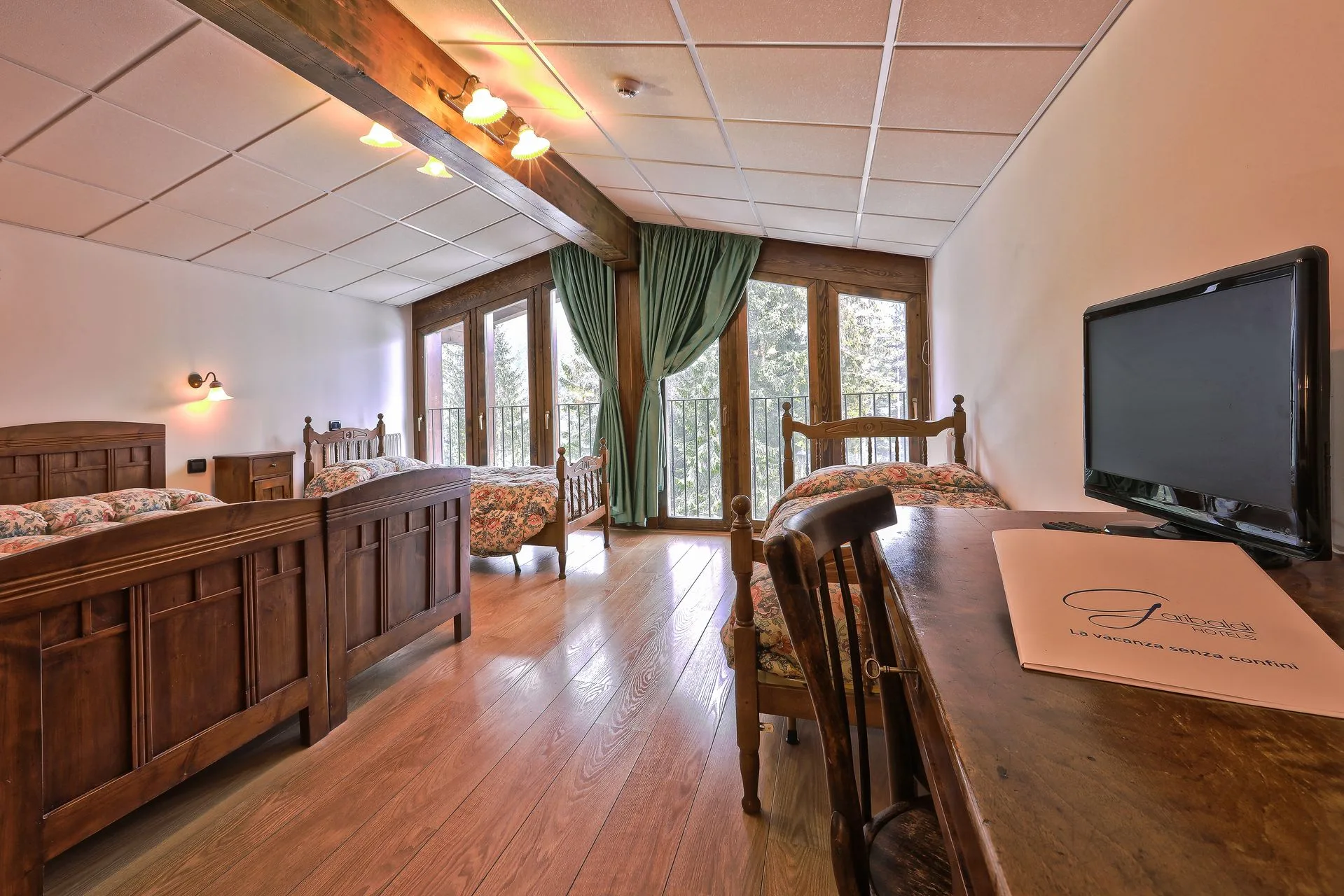 Camera familiare con più letti, parquet e ampie finestre sul bosco