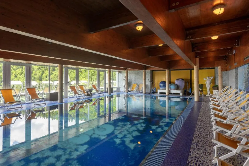 Piscina coperta con lettini e travi in legno affacciata sul verde
