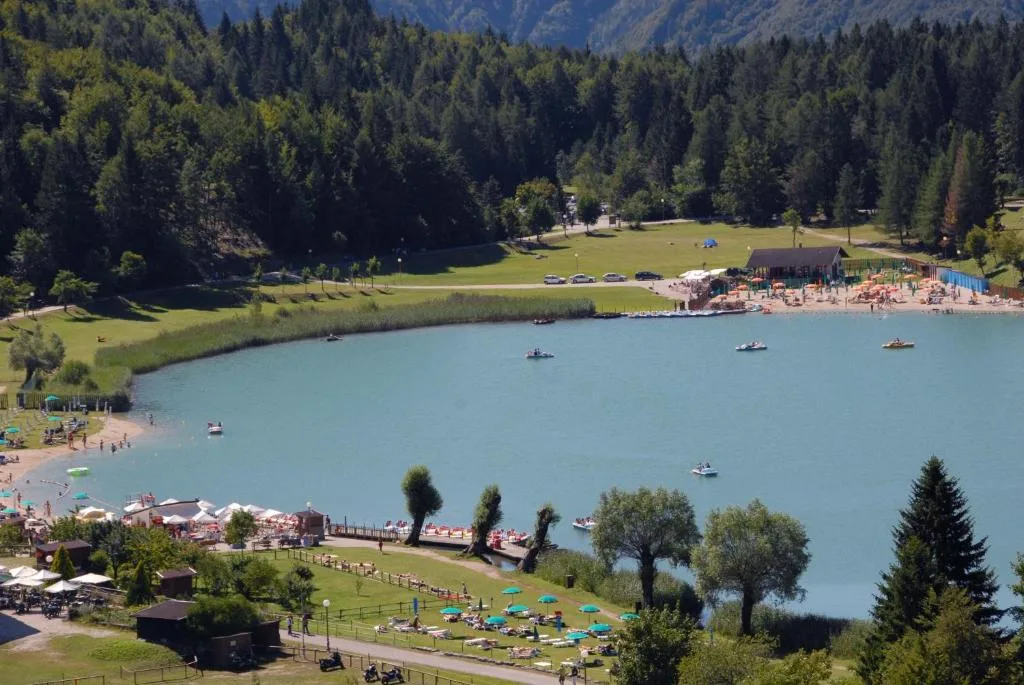 Vista dall'alto del lago alpino con spiaggia, pedalò e area verde