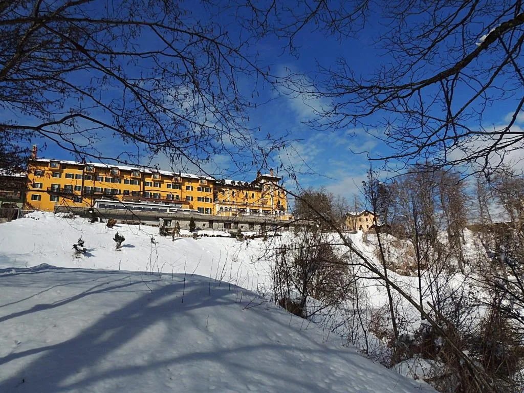Facciata dell'hotel immersa nella neve vista tra i rami spogli