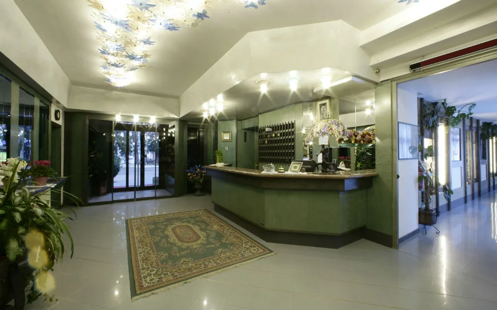 Hall dell'hotel con reception, tappeto e soffitto decorato con lampadario in vetro