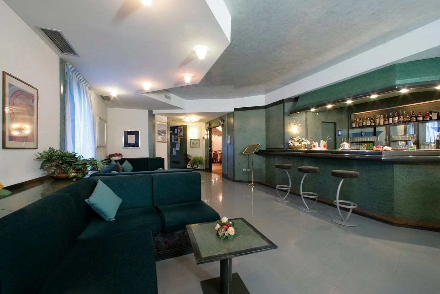Salotto con bar interno, divani verdi e sgabelli, illuminazione soffusa