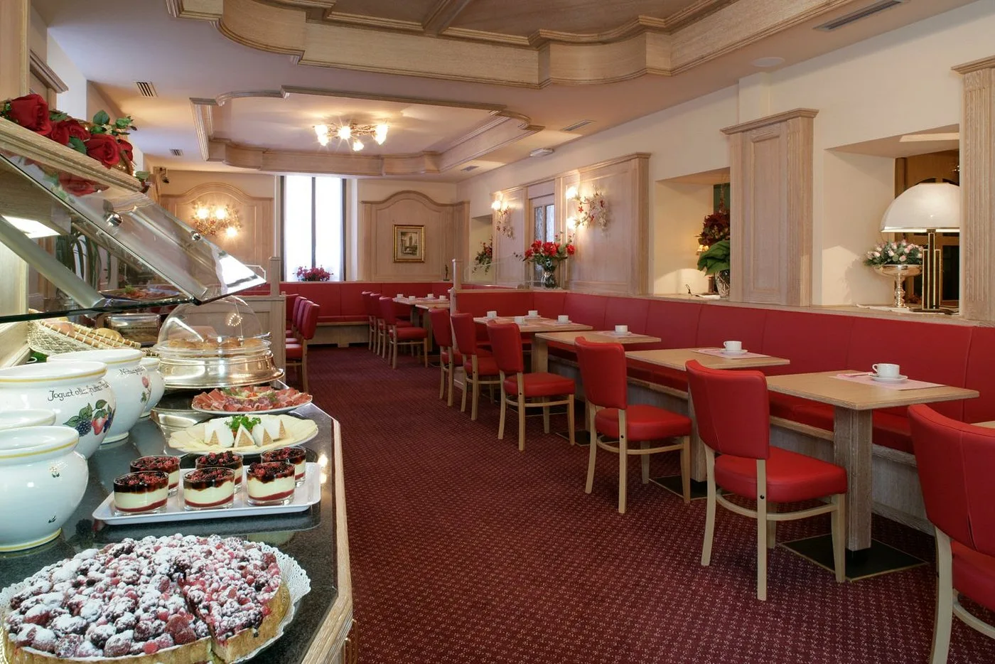 Sala ristorante con buffet di salumi, formaggi e dolci, sedute rosse