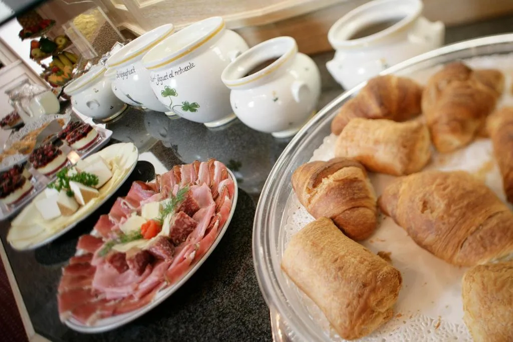 Buffet della colazione con cornetti, salumi, formaggi e brocche in ceramica