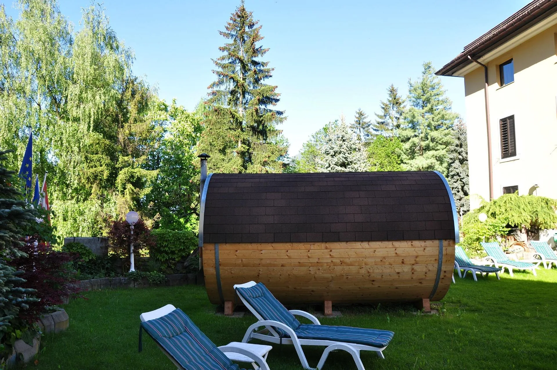 Sauna a botte in legno nel giardino estivo con lettini e alberi