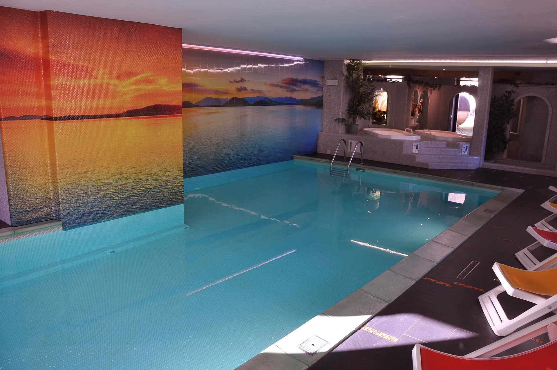 Piscina interna con murale del tramonto sul lago e lettini prendisole