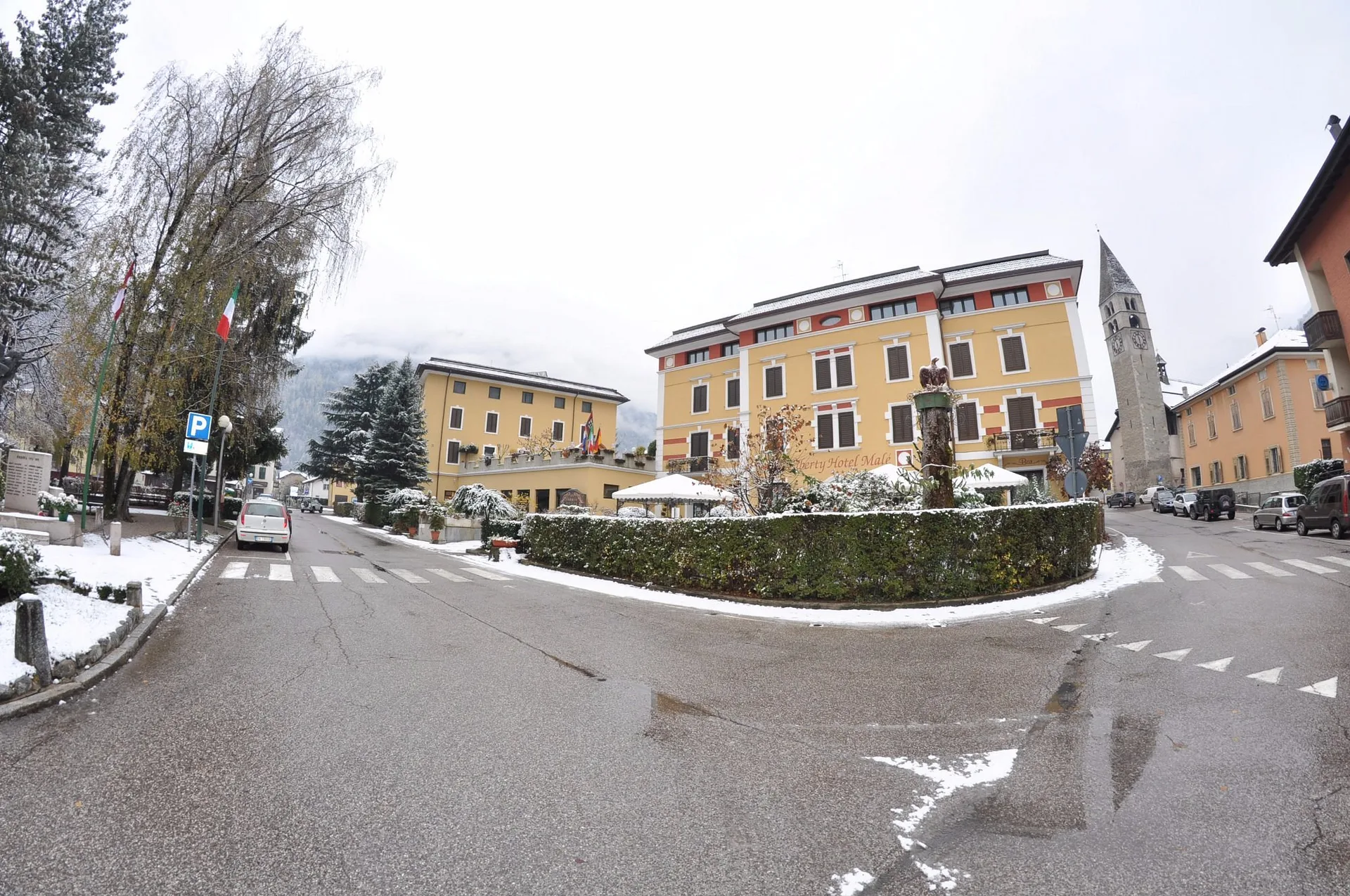 Vista invernale del Liberty Hotel Malè con neve, campanile e piazza