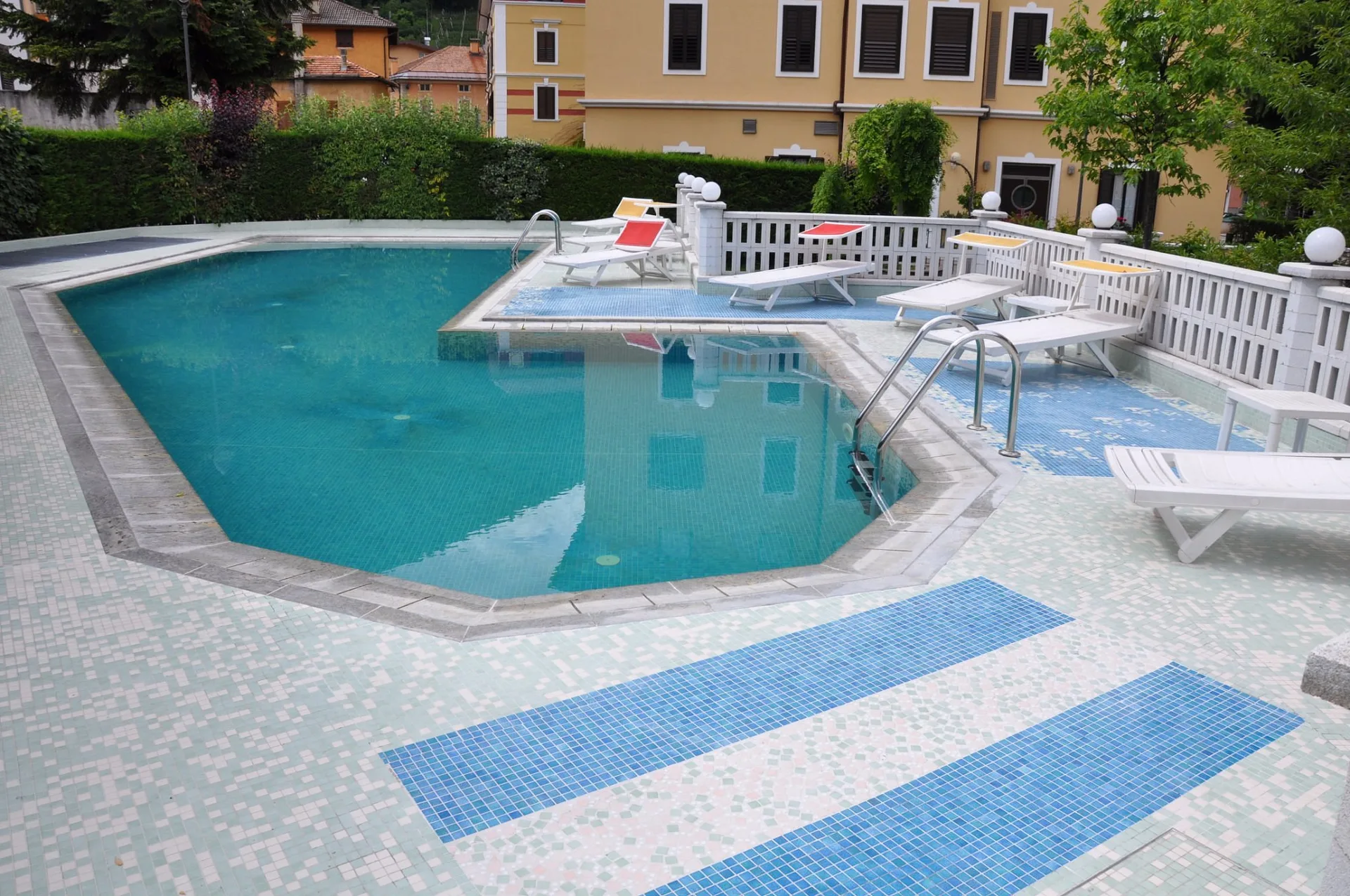 Piscina esterna con lettini e mosaici azzurri accanto alla facciata dell'hotel