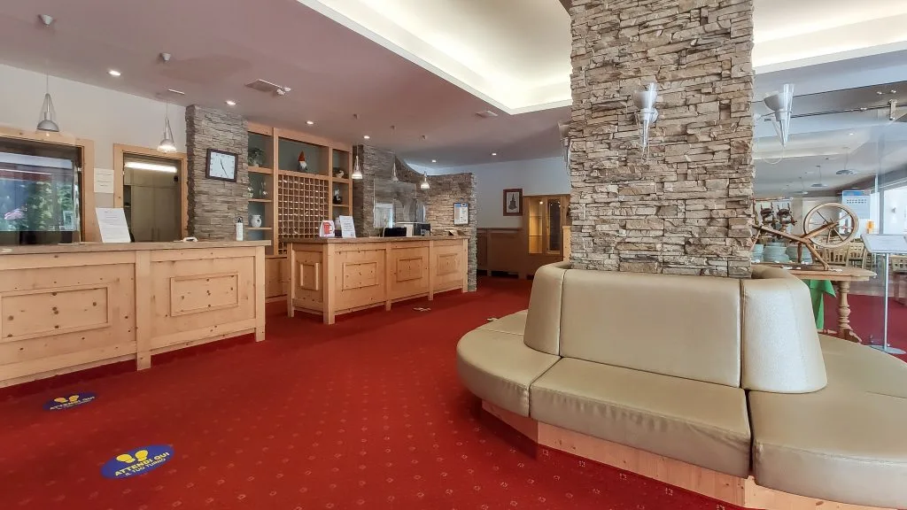 Hall dell'hotel con reception in legno, colonne in pietra e divano curvo