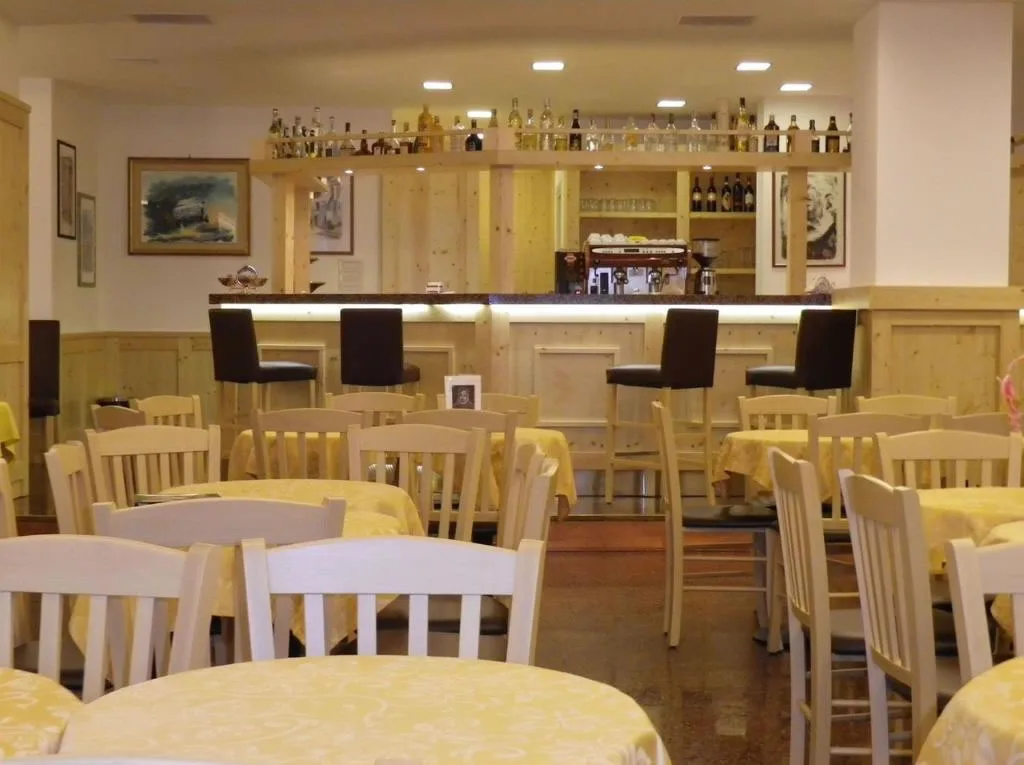 Sala bar dell'hotel con tavoli, sedie chiare e bancone in legno