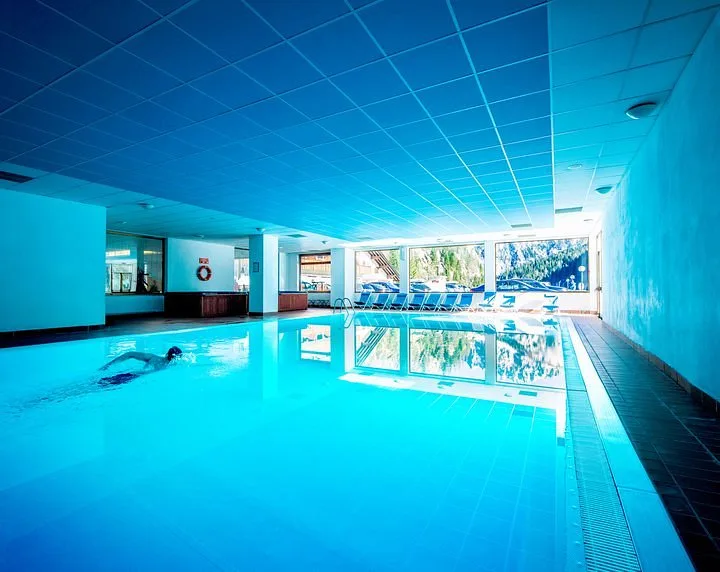 Piscina coperta con nuotatore e ampie vetrate sul paesaggio innevato