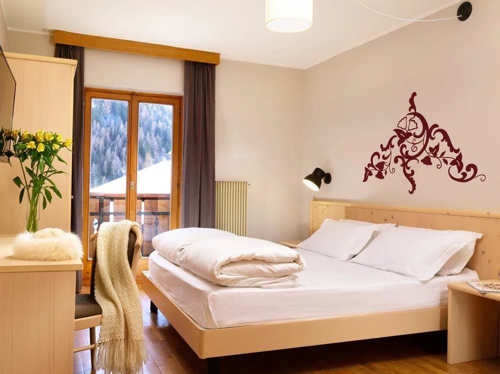 Camera matrimoniale con letto, decorazione floreale a parete e vista sui boschi