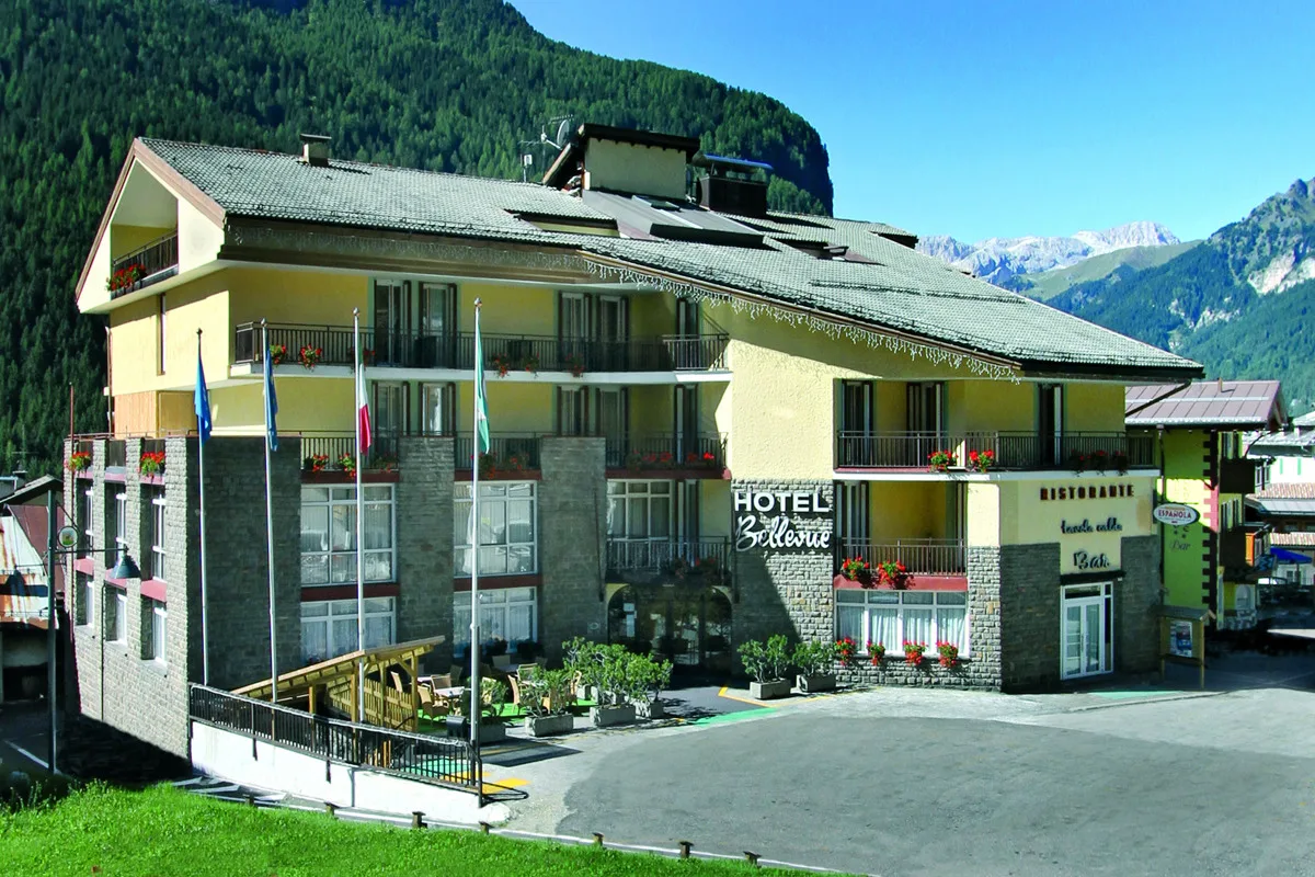 Esterno dell'Hotel Bellevue con bandiere e terrazza attrezzata ai piedi delle montagne